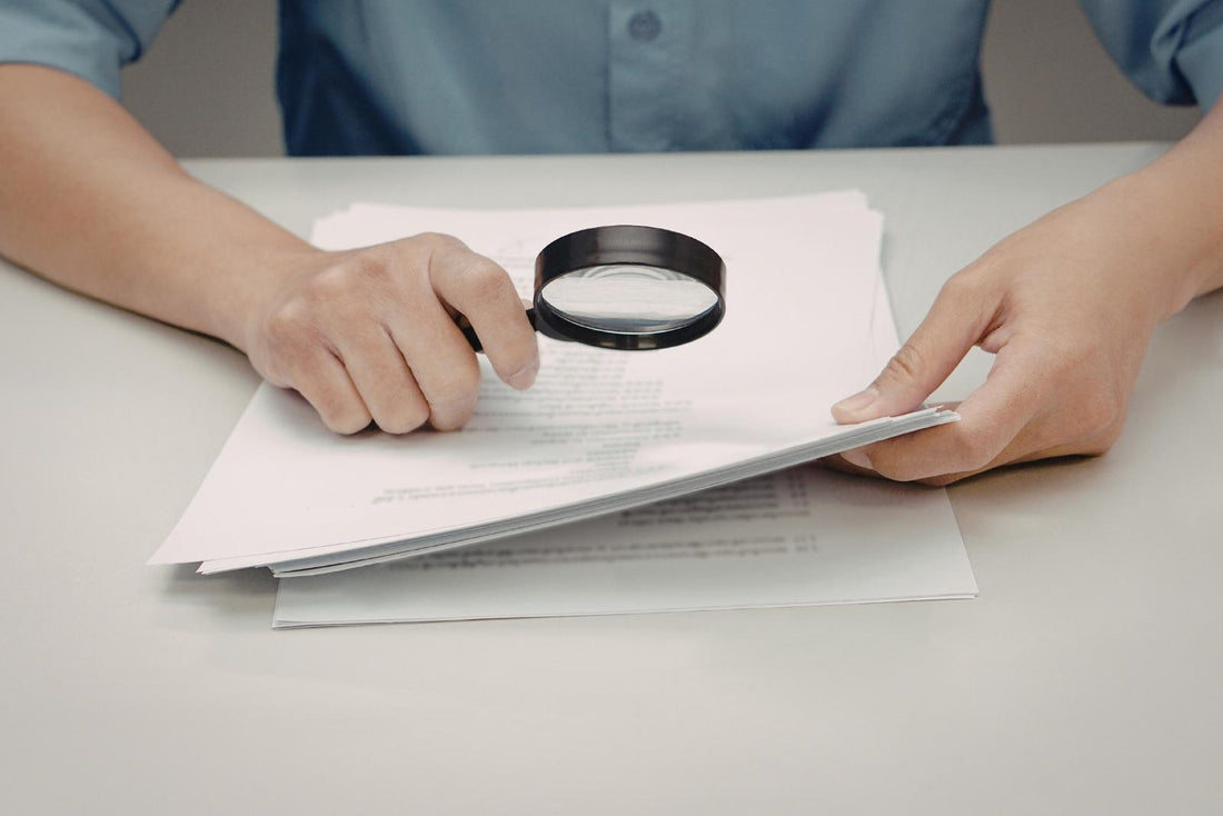 A woman sitting at a desk analyzing medical test results through a magnifying glass. Focused expression, laboratory reports and notes spread across the table, creating an atmosphere of careful health investigation and searching for answers.