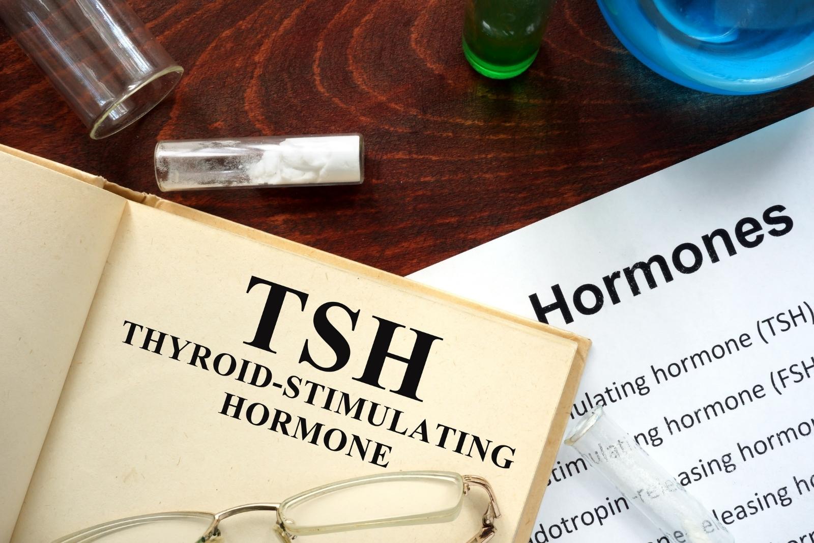 TSH thyroid hormone test documents with hormone analysis papers, eyeglasses, and lab vials on a desk.